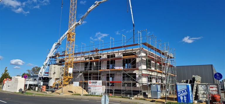 Betonpumpe mit ausgefahrenem Mast über einem eingerüsteten Rohbau bei blauem Himmel