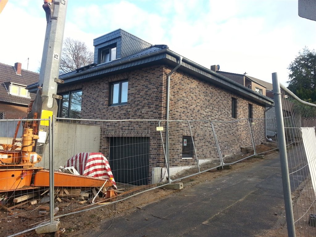 Fertiggestelltes Wohnhaus mit Klinkerfassade und Gaube, von der Straße aus gesehen